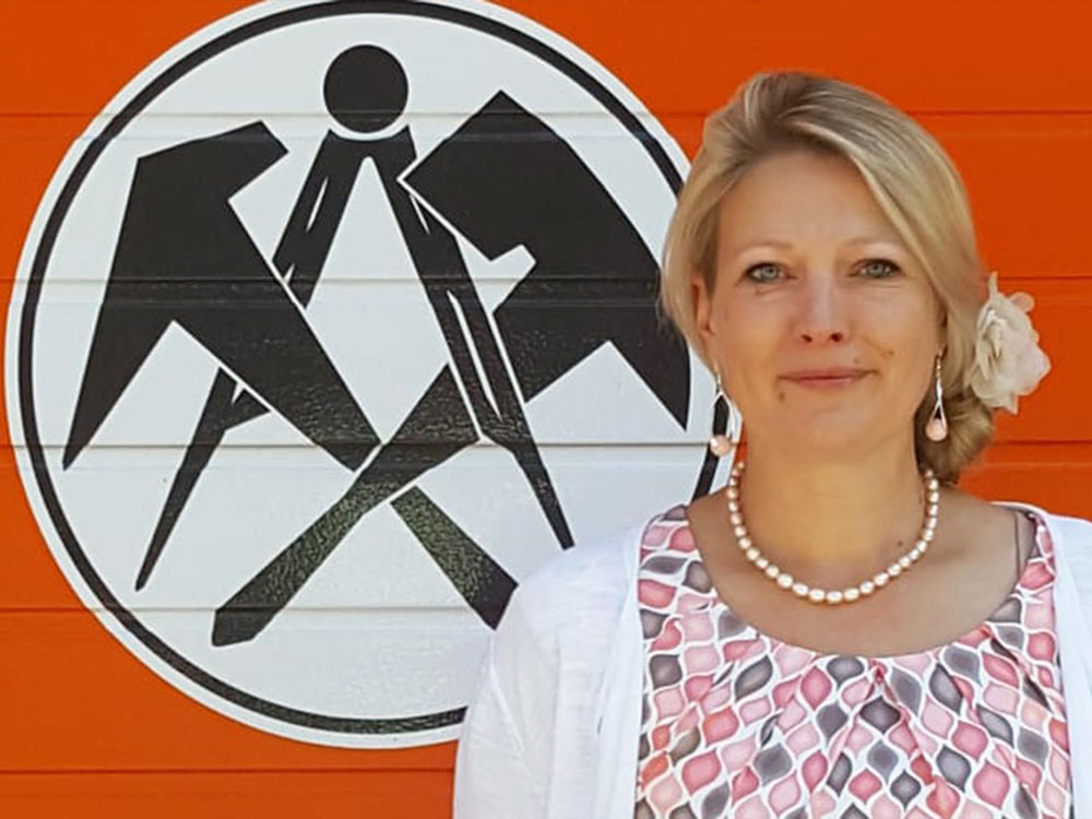 Mitarbeiterin des Dachdeckerbetriebs vor dem Firmenlogo – Organisation und Qualität im Handwerk.