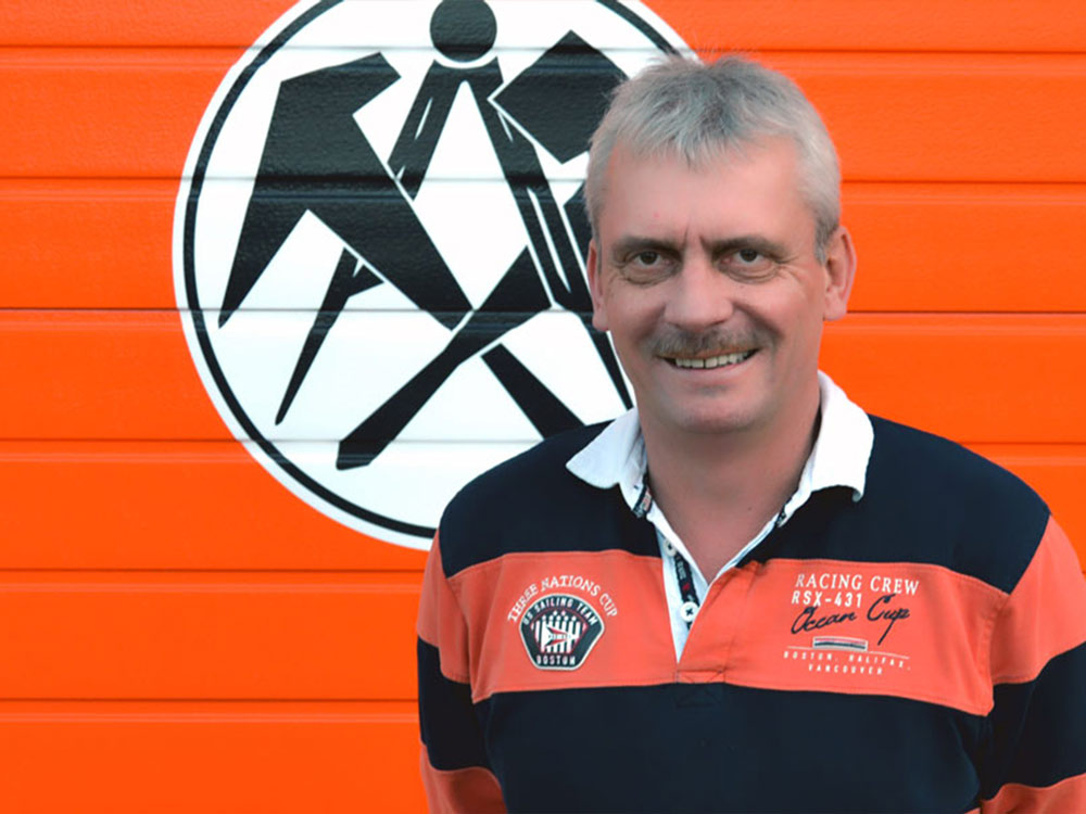 Dachdeckermeister vor Firmenlogo – Erfahrung und Verantwortung im Dachdeckerhandwerk.