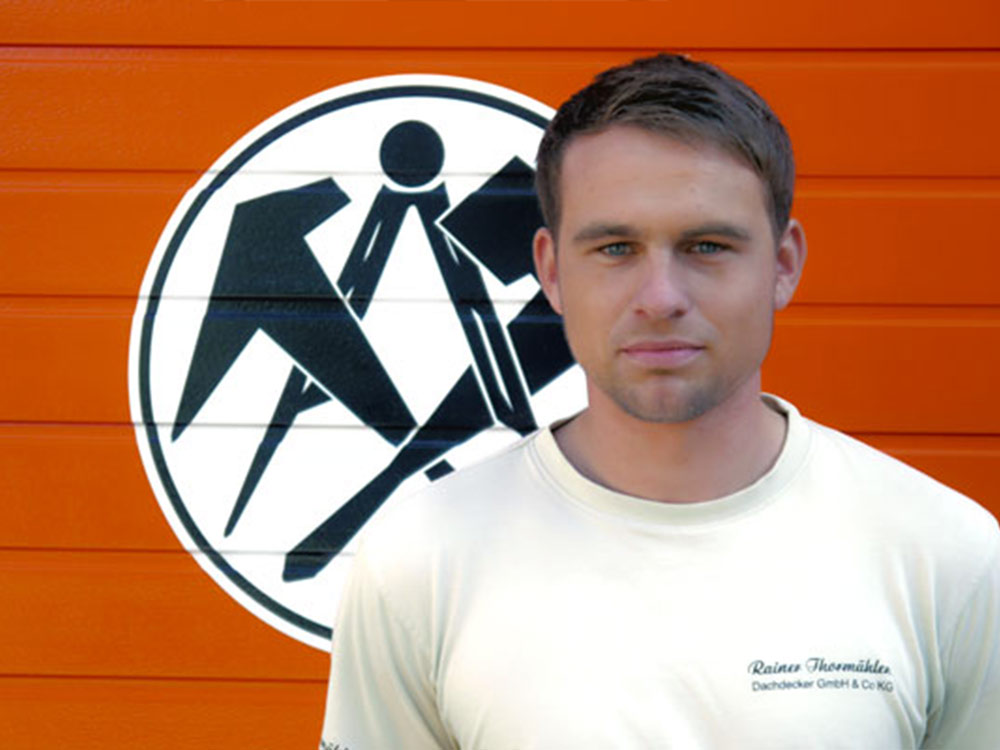 Porträt eines Dachdeckers vor dem Firmenlogo – Handwerksqualität und Teamarbeit im Meisterbetrieb.